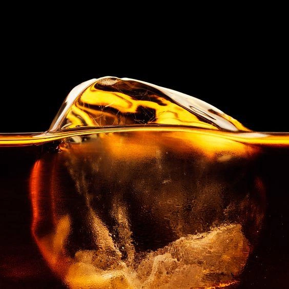 A large ice cube turning in amber whiskey